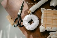 Top view of scissors against coil of twine and textiles with wooden block tied with threads on desk