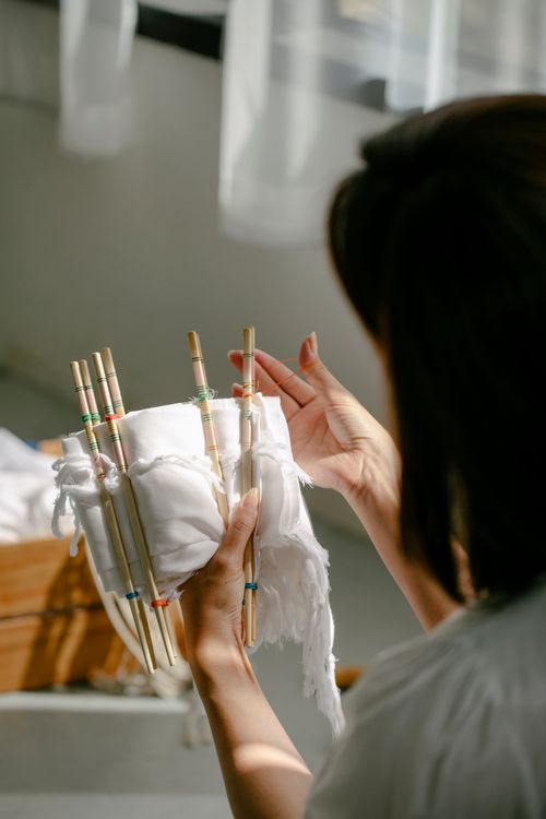 Free Back view of crop anonymous craftswoman wrapping cotton cloth around poles with threads while demonstrating shibori technique in sunlight Stock Photo