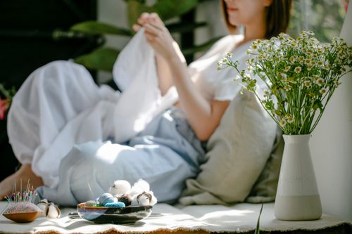 Free Side view of crop anonymous female artisan stitching cotton textile while showing shibori technique against blossoming flowers in vase Stock Photo
