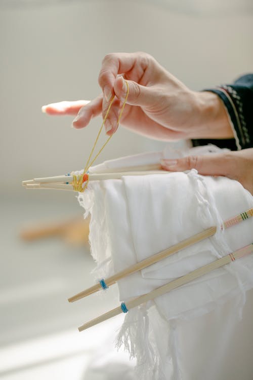 Crop anonymous female artisan tying threads on poles with cotton cloth while showing shibori technique on sunny day