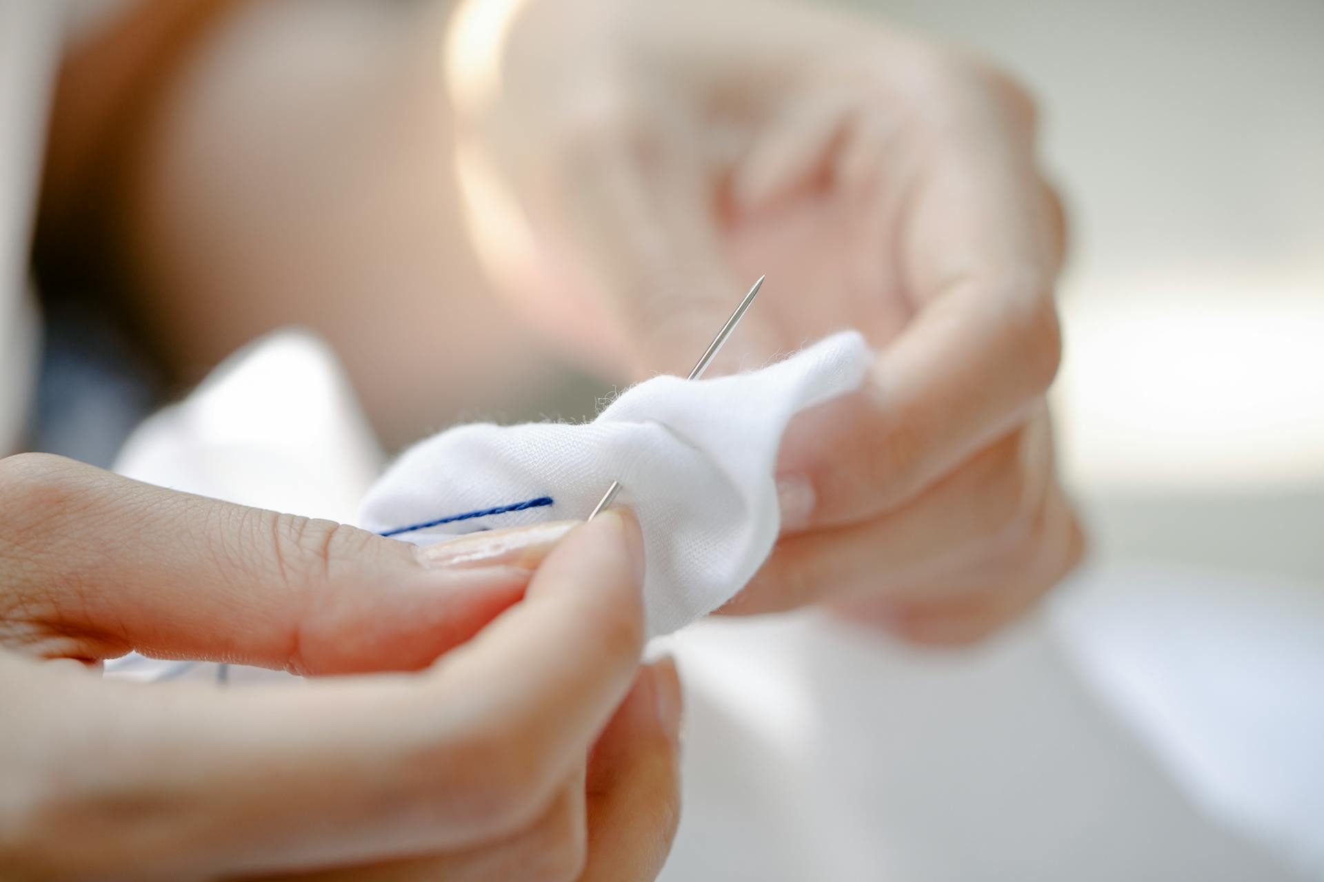 Closeup of crop anonymous female artisan threading needle into cotton fabric while showing Japanese tie dye technique in sunshine