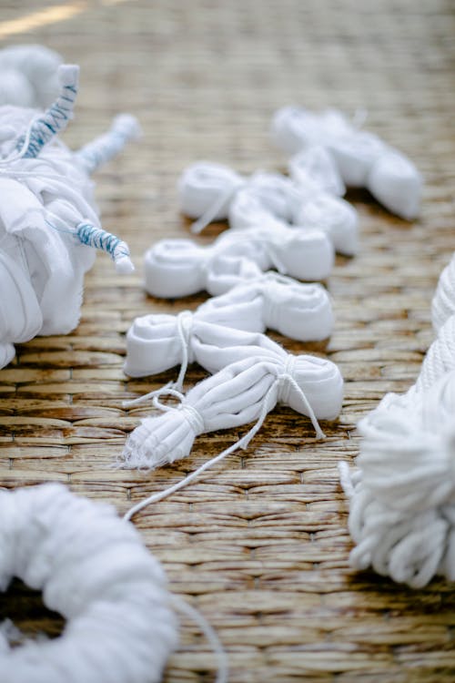 Folded cotton clothes tied with threads representing various shibori techniques on wicker surface in sunlight