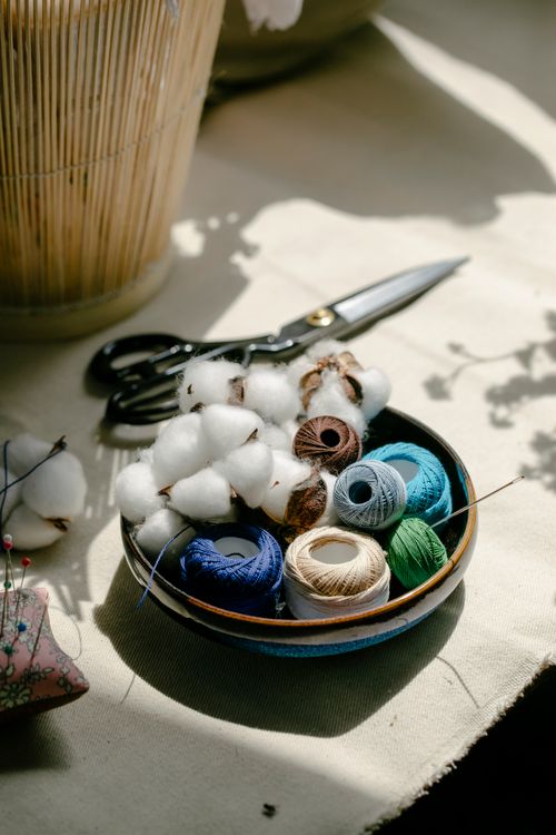 Free From above of spools of colorful threads and cotton balls in bowl placed on table with needle pillow and scissors in workshop Stock Photo