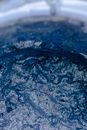 Closeup of vessel filled with blue water with drops and ripple on surface