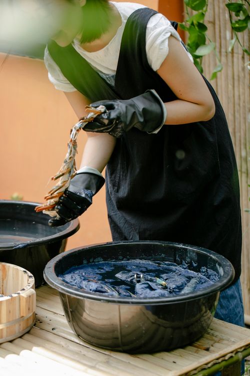 Free Crop Asian craftswoman with pins on folded textile demonstrating tie dye technique above basin with painted water Stock Photo