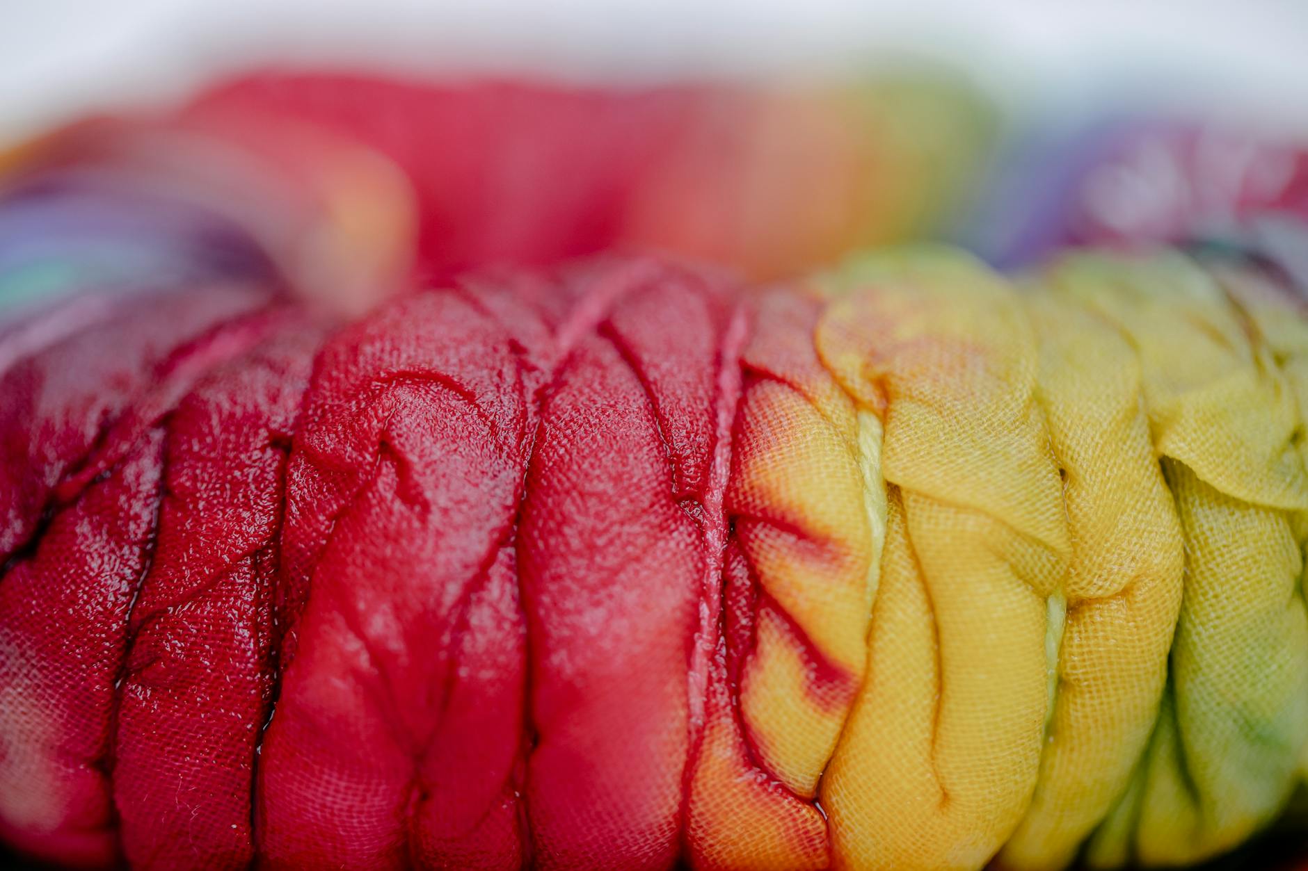 Closeup of pleated cloth with colorful paints and threads representing Japanese tie-dye technique on blurred background