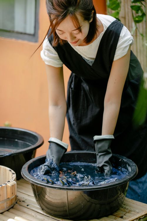 Free Crop Asian craftswoman leaning forward while painting textile in basin with aqua and showing shibori technique outdoors Stock Photo