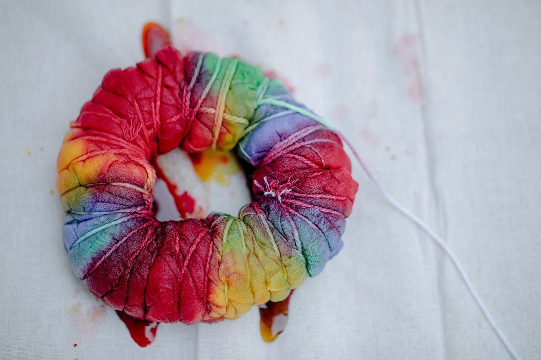 Top view of pleated textile with multicolored paints tied with threads representing Japanese tie dye technique