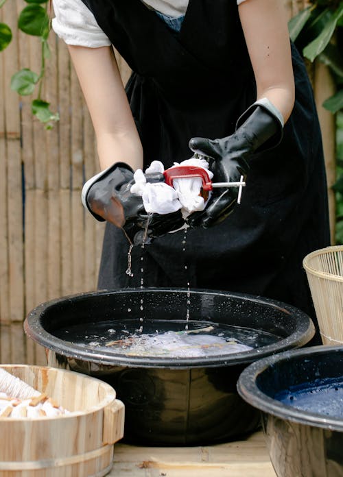 Crop anonymous female artisan squeezing fabric with clamp above basin with water while demonstrating tie dye technique outdoors