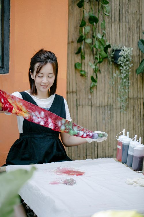 Free Asian woman enjoying tie-dyeing at an indoor table, surrounded by plants. Stock Photo