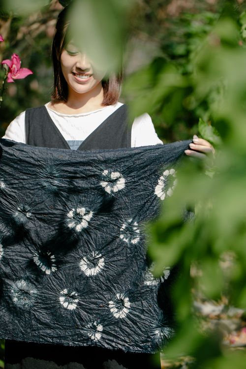 Free Asian woman holding a black and white tie-dye cloth while smiling in a lush garden. Stock Photo