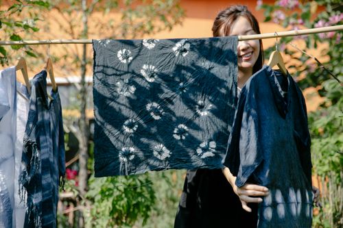 Free Young woman showcasing tie-dye clothes drying on a clothesline outdoors. Stock Photo
