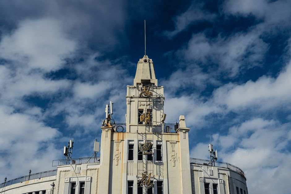 Photo by Clam Lo Exterior of building with small windows and tower located against blue sky with clouds on street in city with bright sunlight