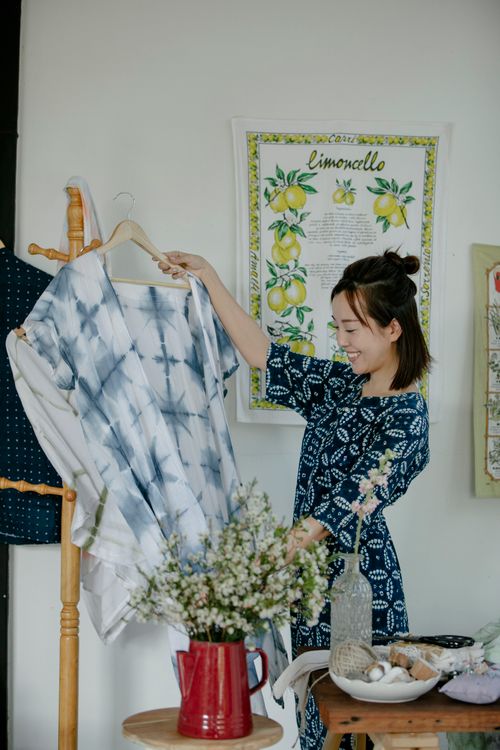 Free Smiling young woman displays a handmade tie-dye dress in a cozy home setting. Stock Photo