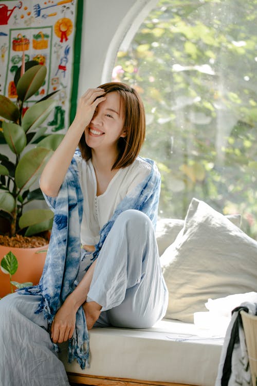 Smiling ethnic woman covering face while sitting near window