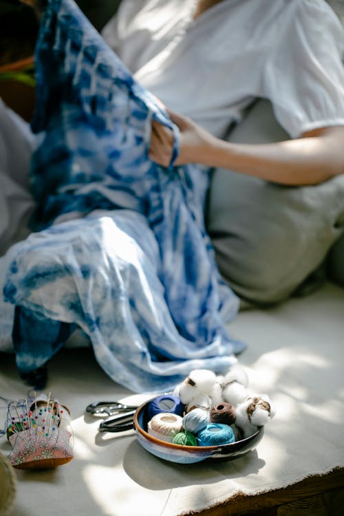 High angle of crop female dressmaker sitting on cushion with fabric painted with Japanese technique shibori in workshop