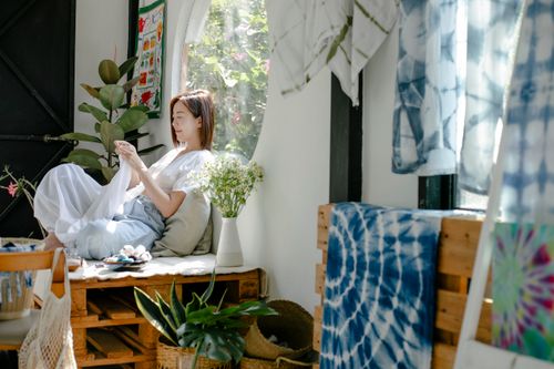 Free Side view of positive ethnic female tailor sewing cloth while working in creative atelier with tie dyed fabrics Stock Photo