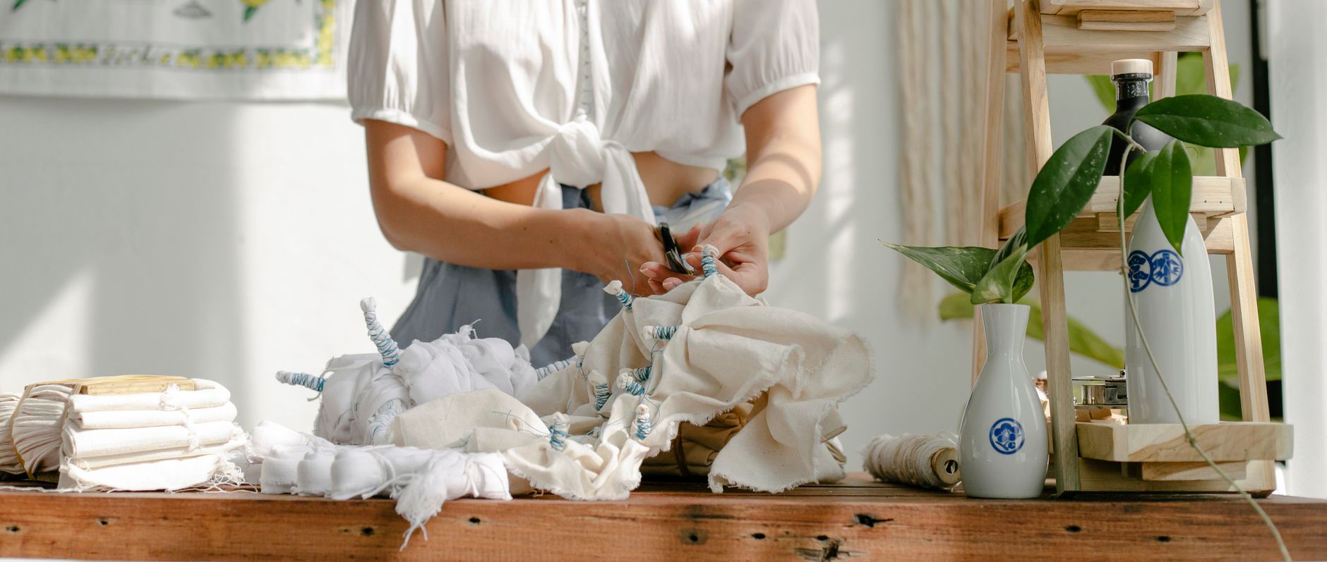 Unrecognizable female master standing at wooden table with white fabric while preparing for shibori dyeing in workshop with professional tools