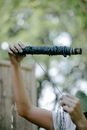 Unrecognizable skilled person winding thread on wooden stick while preparing for shibori dyeing against tall green plants on blurred background