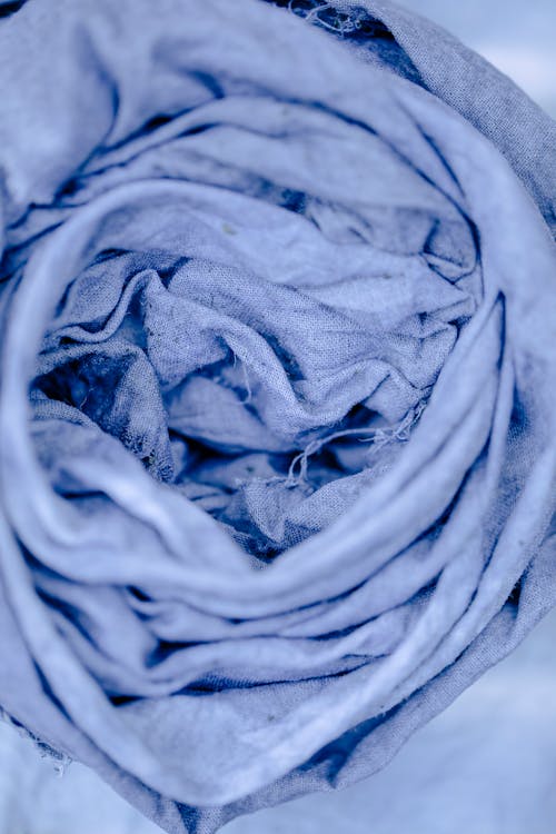 Top view of creased rolled linen textile with threads dyed in blue color placed on surface in light modern workshop