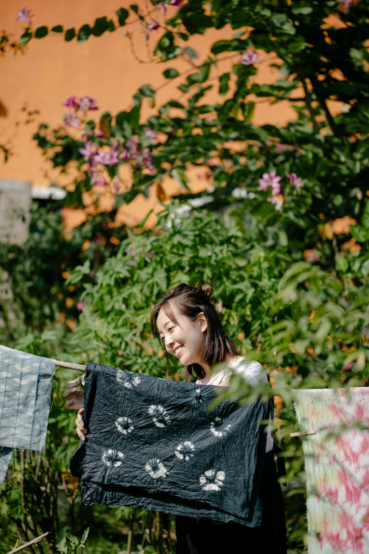 Joyful Asian Woman Near Rope With Painted Fabrics