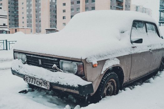 A classic car covered in snow, parked in a residential area in Saint Petersburg, Russia.