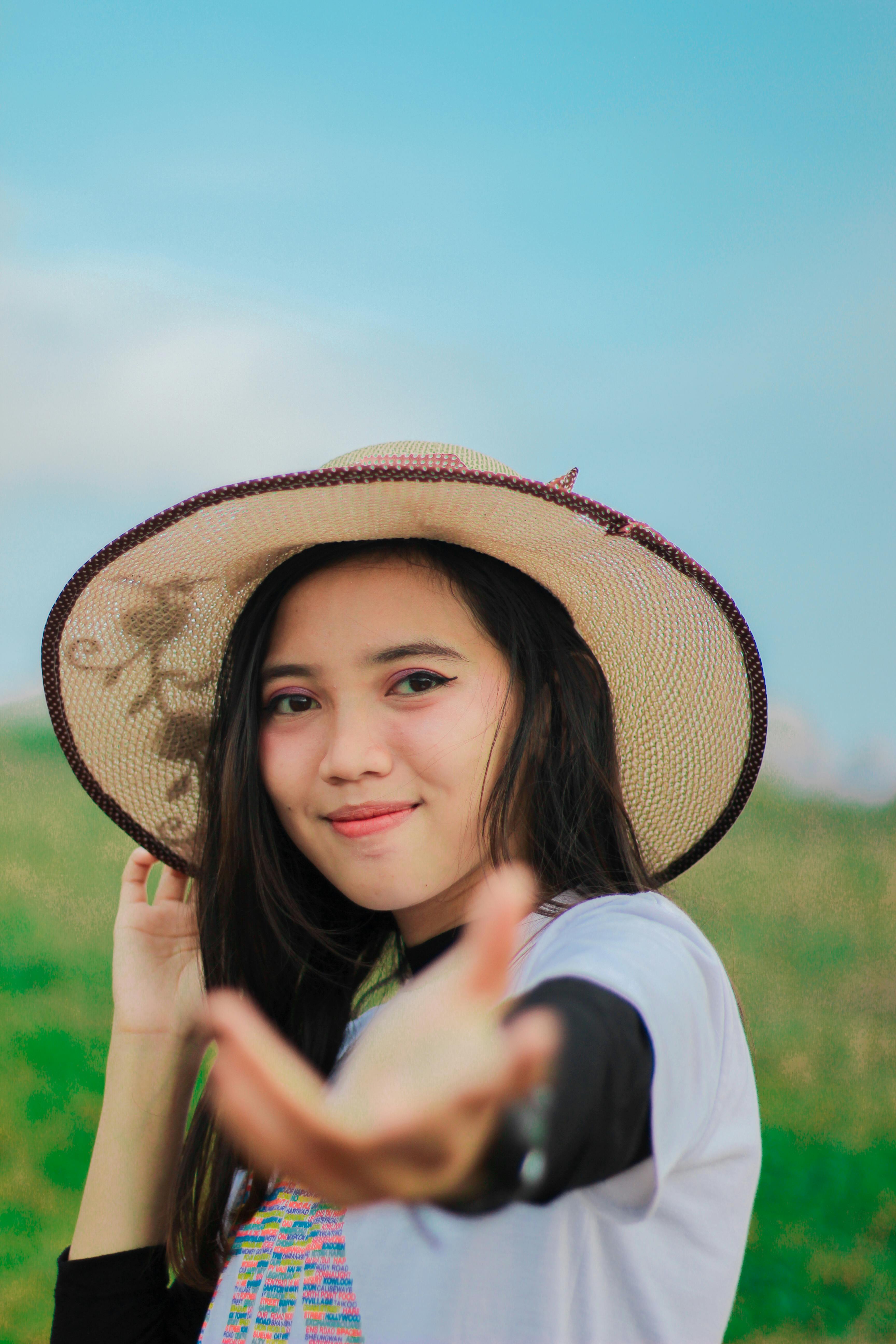 Free Smiling Asian woman wearing a straw hat enjoys a sunny day outdoors. Stock Photo