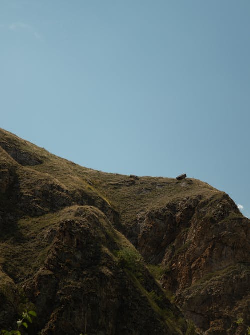 Scenery of rocky rough mountainous terrain covered with grass against cloudless blue sky