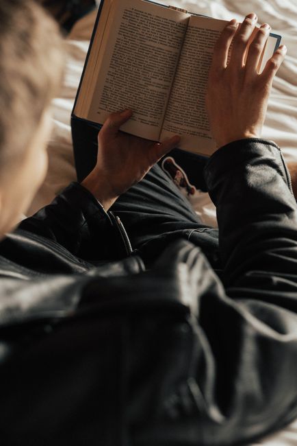 Comfortable reading moment captured from above, showcasing a person in a leather jacket engaged with a book.
