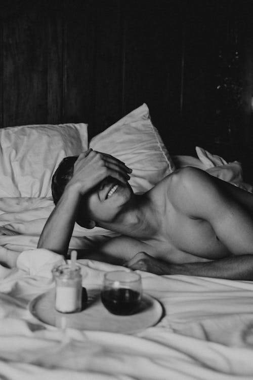 Grayscale Photo of a Shirtless Man Lying on Bed