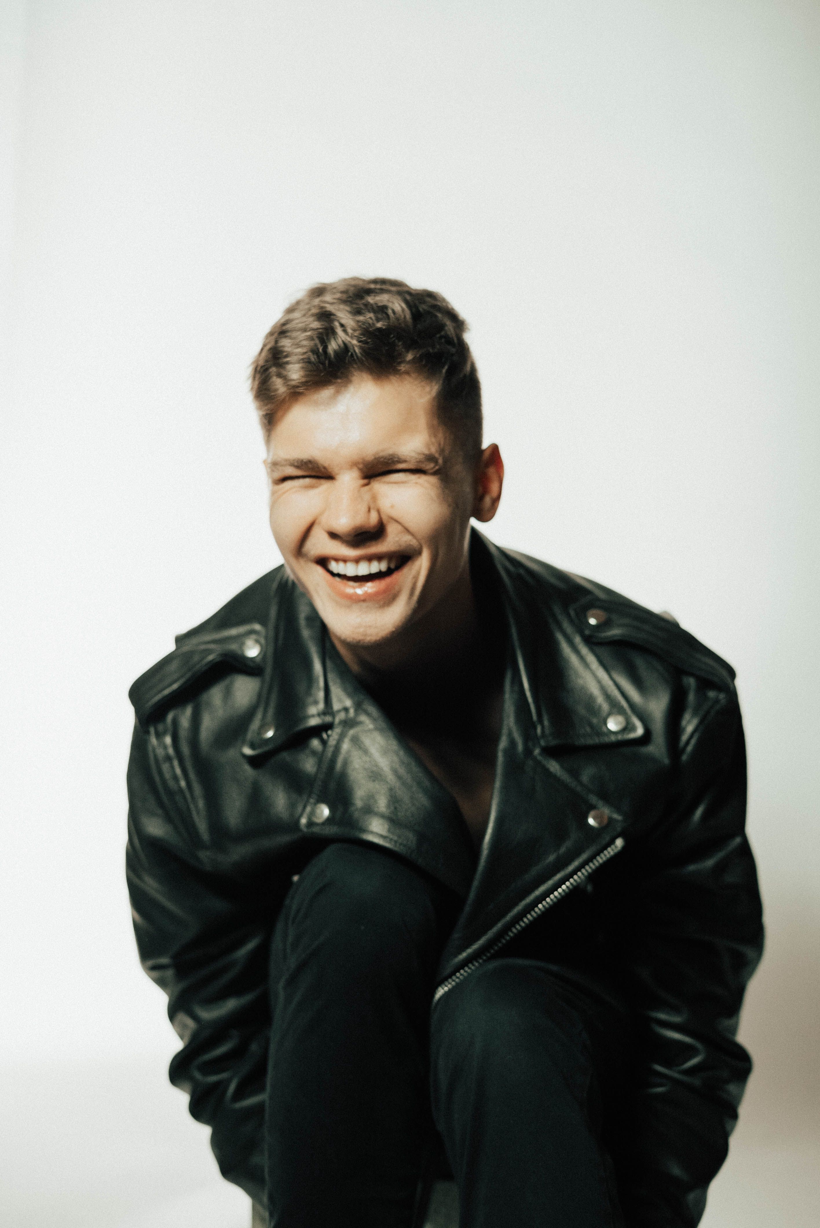 Portrait of a cheerful man in a black leather jacket, laughing with joy against a white background.