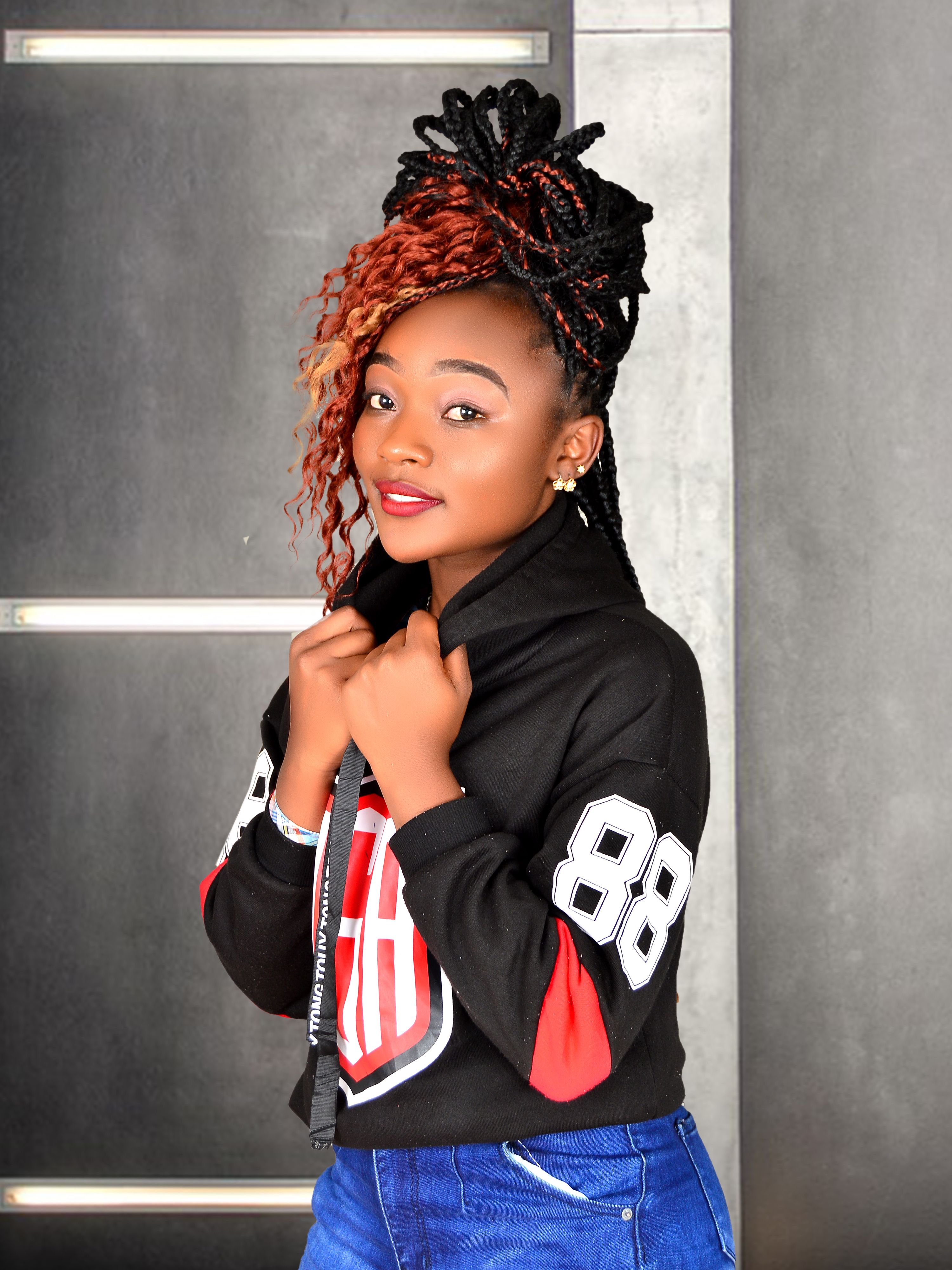 Portrait of a stylish young woman with braided hair wearing a printed hoodie and jeans indoors.