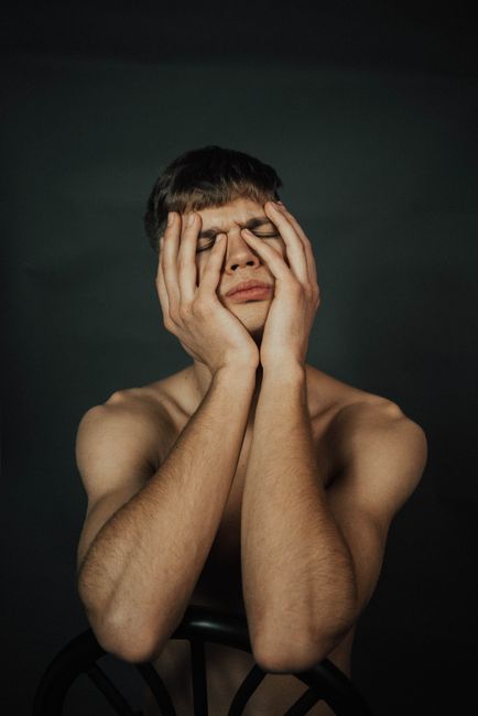 Artistic portrait capturing a shirtless young man deep in thought, hands over face.