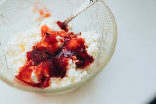 From above of appetizing cottage cheese with berry jam served in glass bowl with spoon on white table
