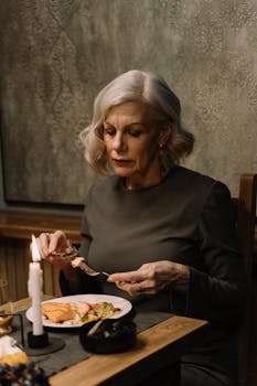 Senior woman with gray hair dining elegantly by candlelight indoors.