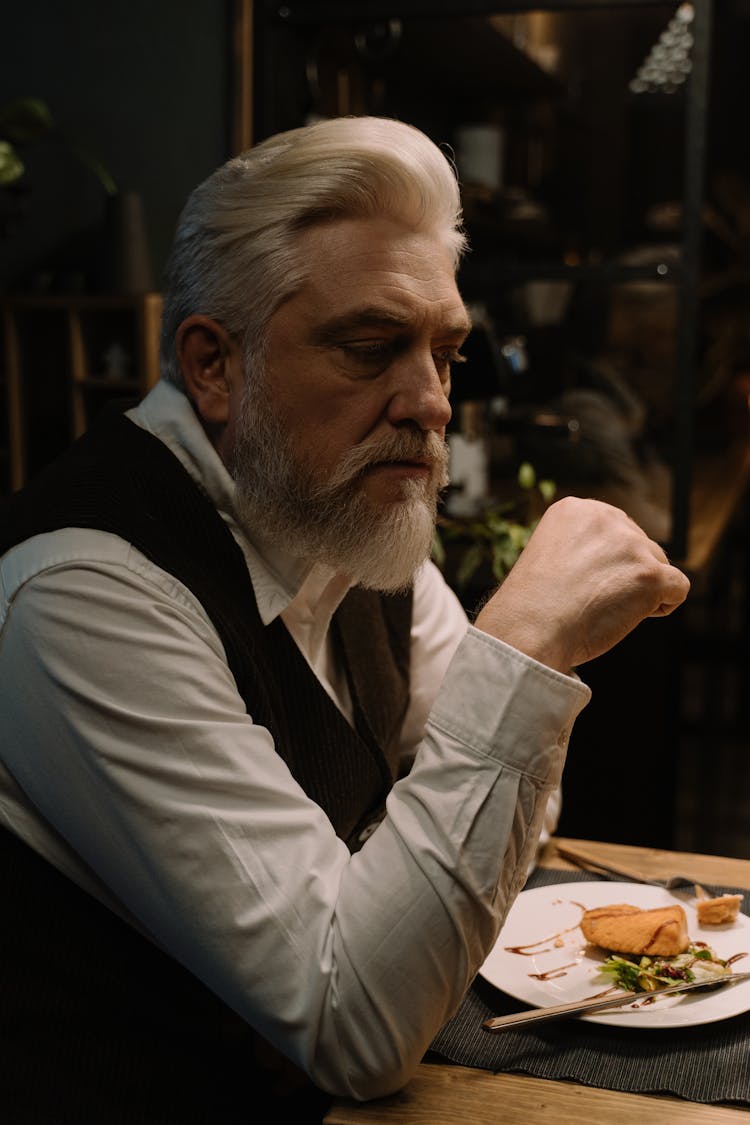 A Bearded Man In A Vest Having Dinner