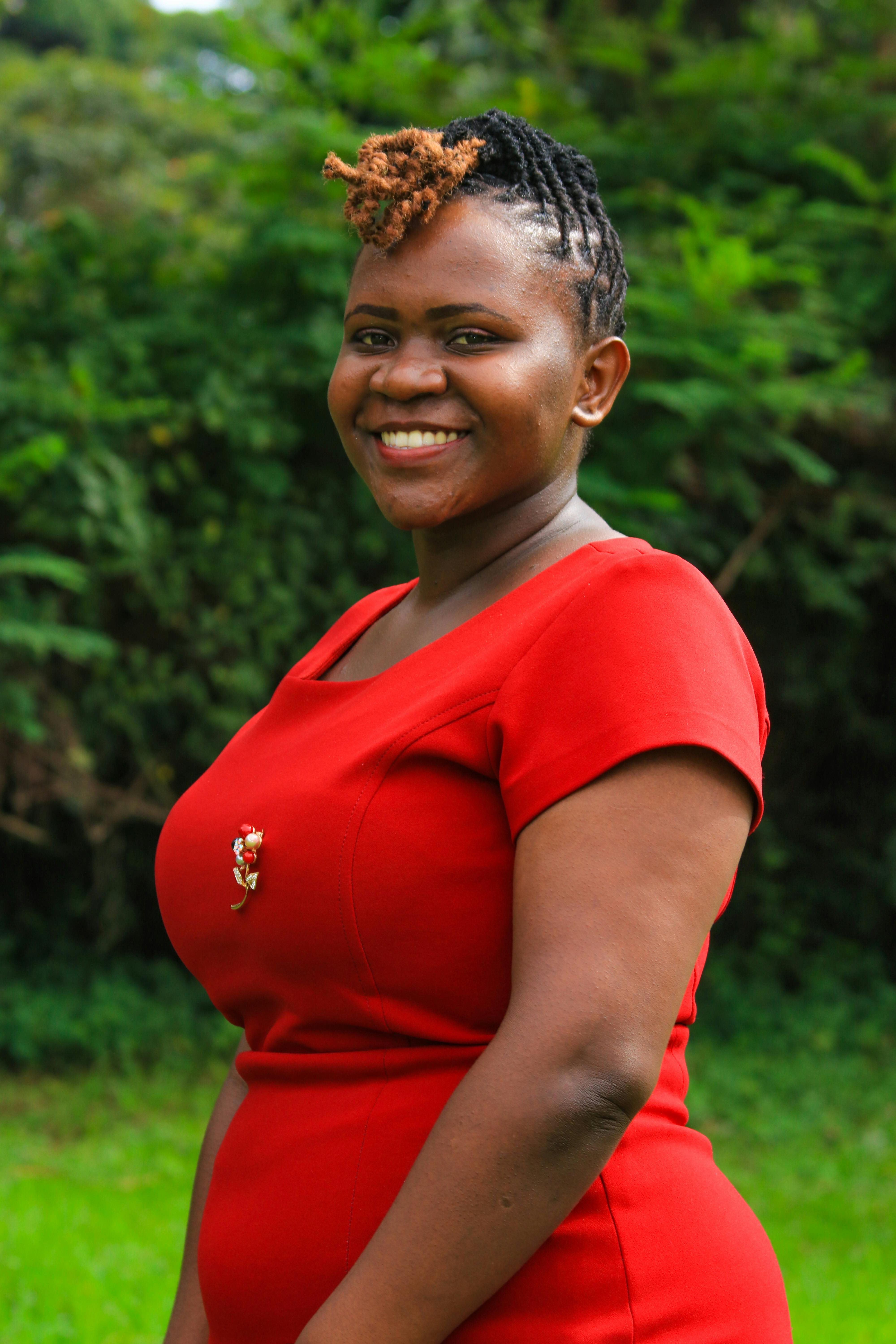 An African American woman smiling in a red dress in a lush outdoor setting.