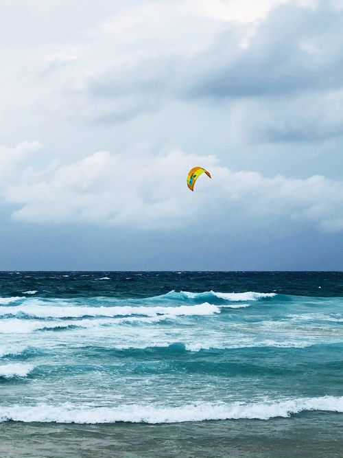 Free A vibrant kite soars above waves and cloudy skies, capturing the thrill of kitesurfing by the sea. Stock Photo