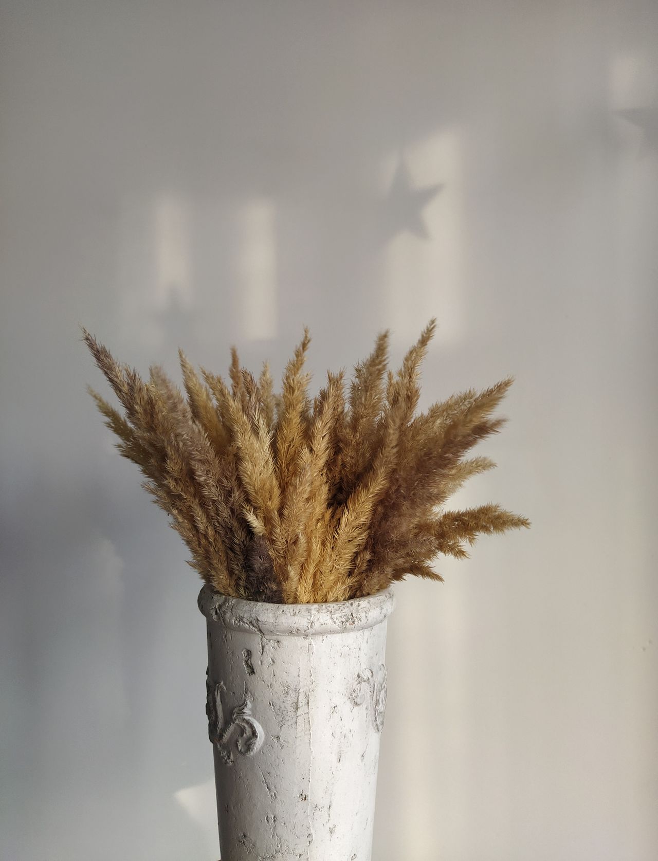 Golden dried grass bouquet in a distressed white vase against a light wall