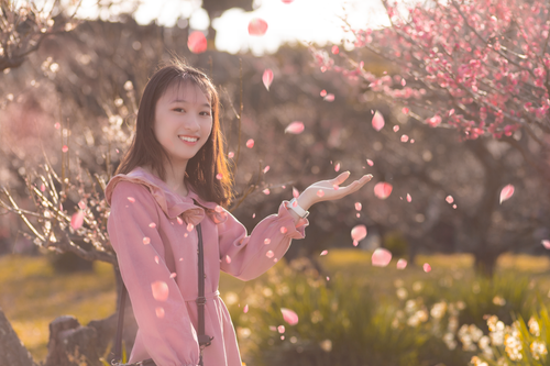 Free A smiling teenage girl enjoying pink cherry blossom petals outdoors on a sunny spring day. Stock Photo