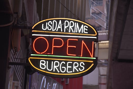Close-up of a neon sign for USDA Prime burgers, glowing at night on a city street.