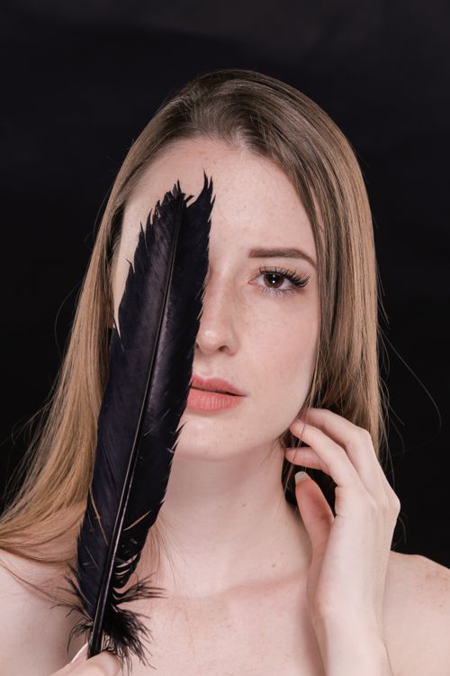 Free Close-up portrait of an elegant woman holding a dark feather against a black background. Stock Photo