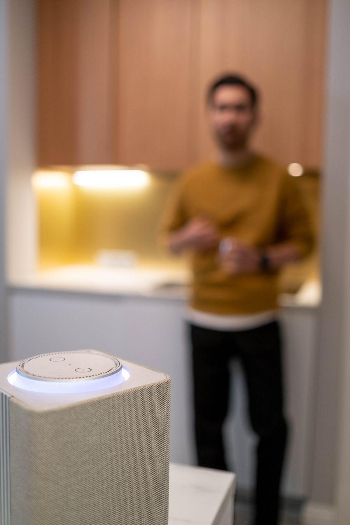 A man speaking to a smart speaker on a kitchen counter