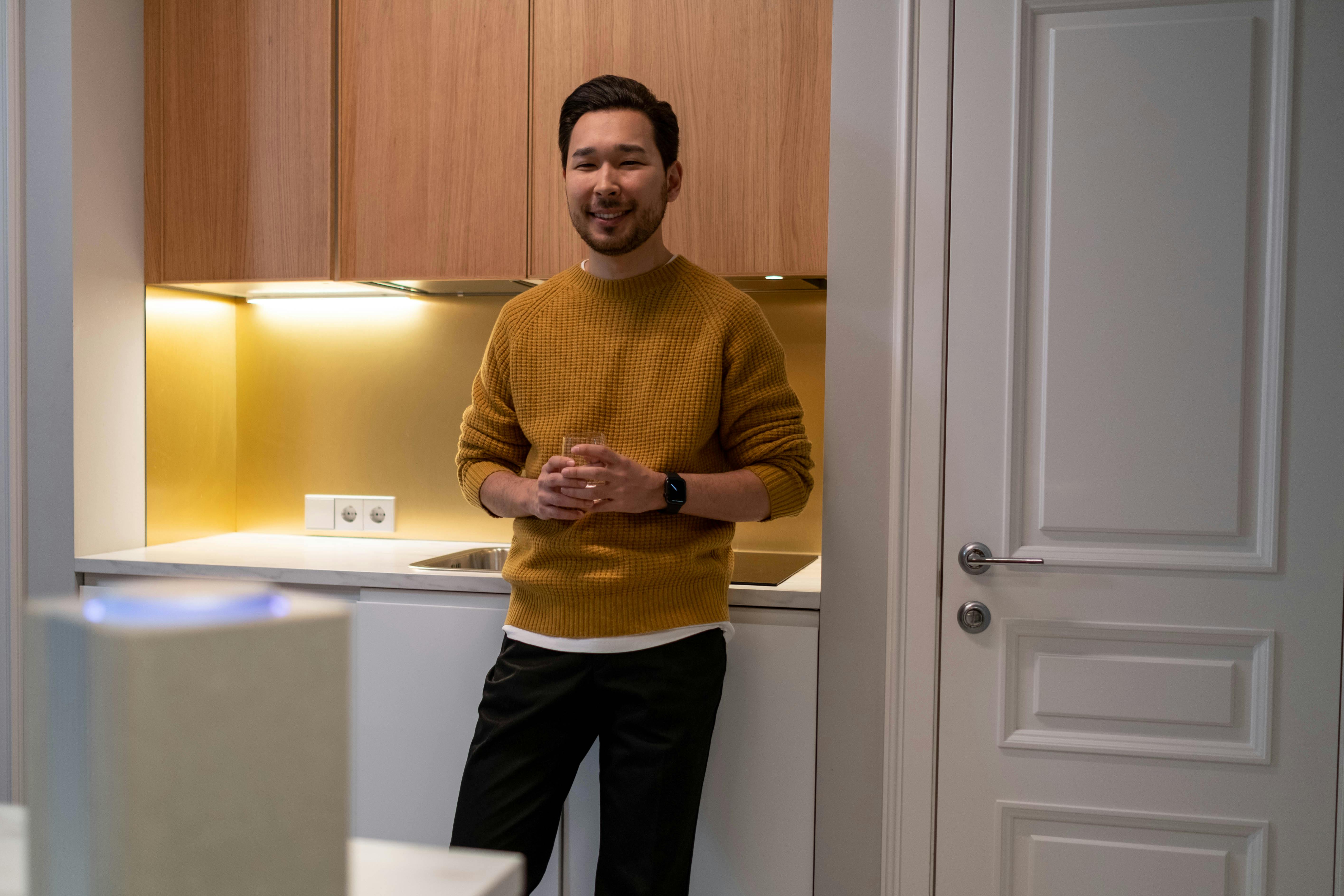 man in yellow knit sweater and black pants standing near white wooden door