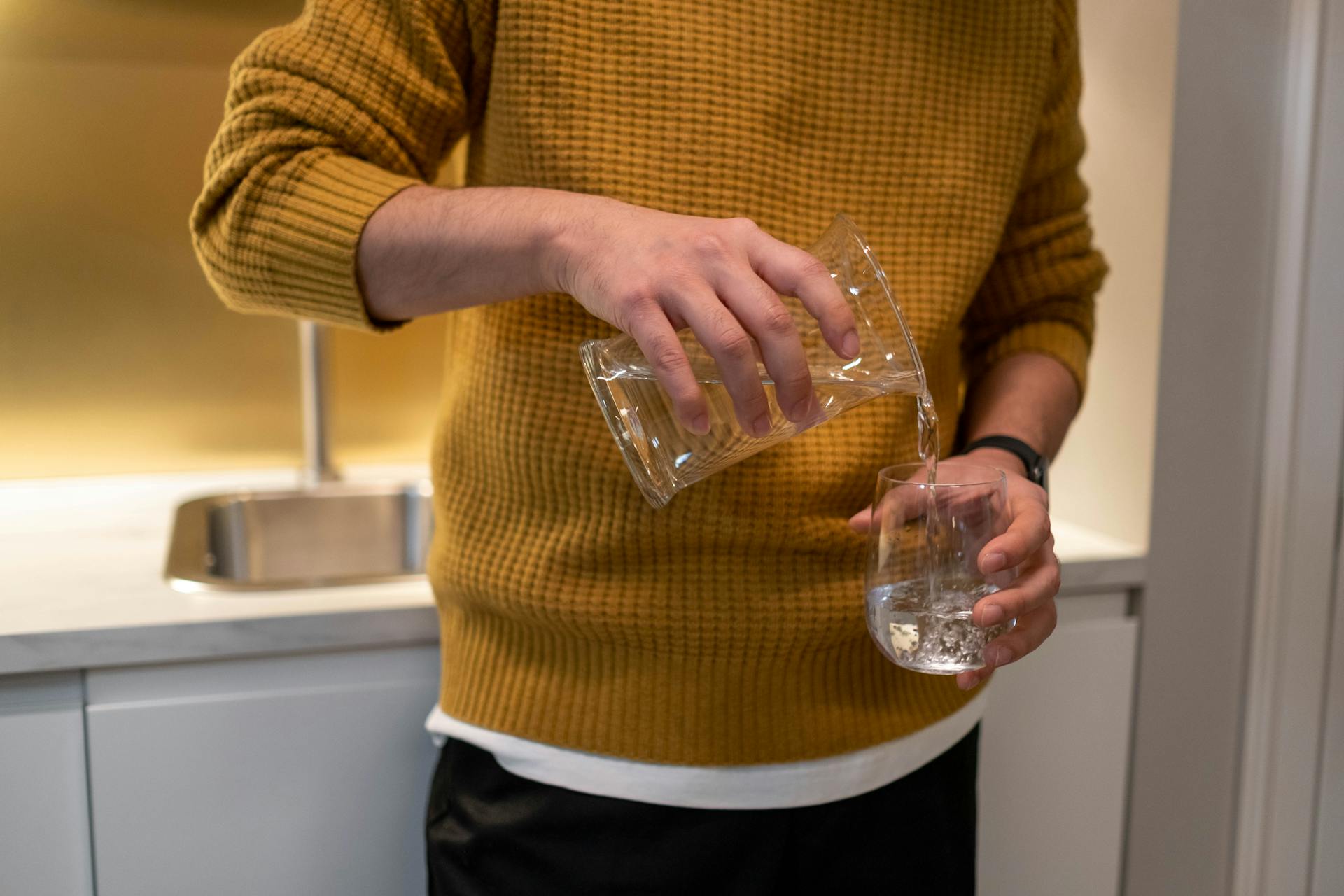 Person in Yellow Knitted Sweater Pouring Water in the Clear Glass