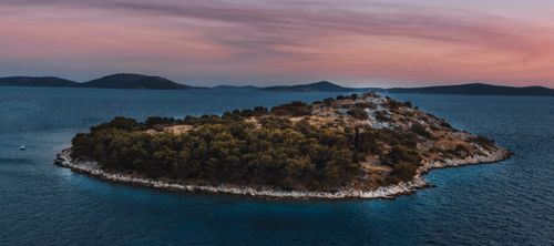 Free Tranquil island surrounded by calm sea waters at sunset, creating a picturesque seascape. Stock Photo