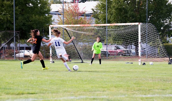 Women athletes competing in a lively soccer game with a goalkeeper defending the goal.