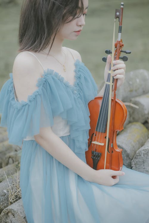 Free Woman in a Blue Dress Looking at  Her Violin Stock Photo