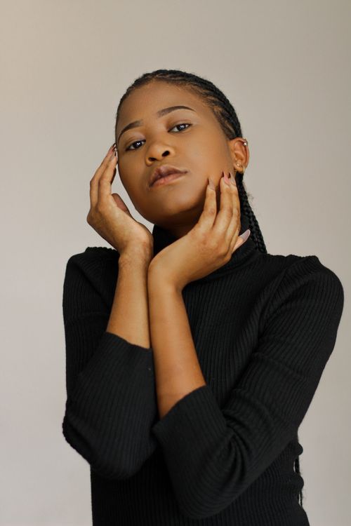 Free Studio portrait of a confident woman posing with hands on face in black turtleneck. Stock Photo