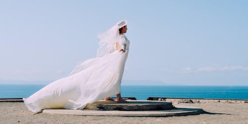 Woman in White Bridal Gown Standing in Brown Round Concrete Surface Under Blue Sky during Day Time